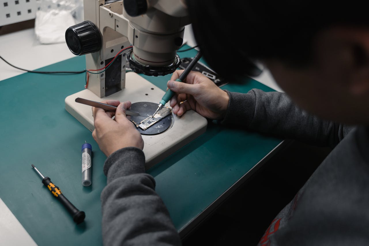 Crafting Captivating Headlines: Your awesome post title goes here Technician using a microscope to repair a broken electronic board with precision tools.
